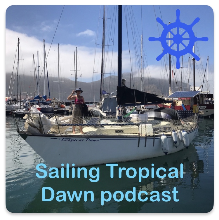 Image of a sailboat with a woman standing on the deck (Kay) text at bottom: Sailing Tropical Dawn podcast and top right a sailboat steering wheel